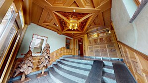 Eine prächtige Treppe mit hölzernen Geländern und einer Chandelüster, die zu einem Raum mit geschnitzten Holzvertäfelungen und einem großen Spiegel führt.