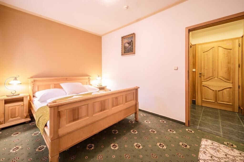 A bedroom with a wooden bed, nightstands with lamps, a door, and a patterned carpet.