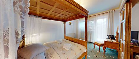 Una cama con dosel y tablero de madera, una mesita de noche con lámpara, y un televisor sobre un atril de madera.