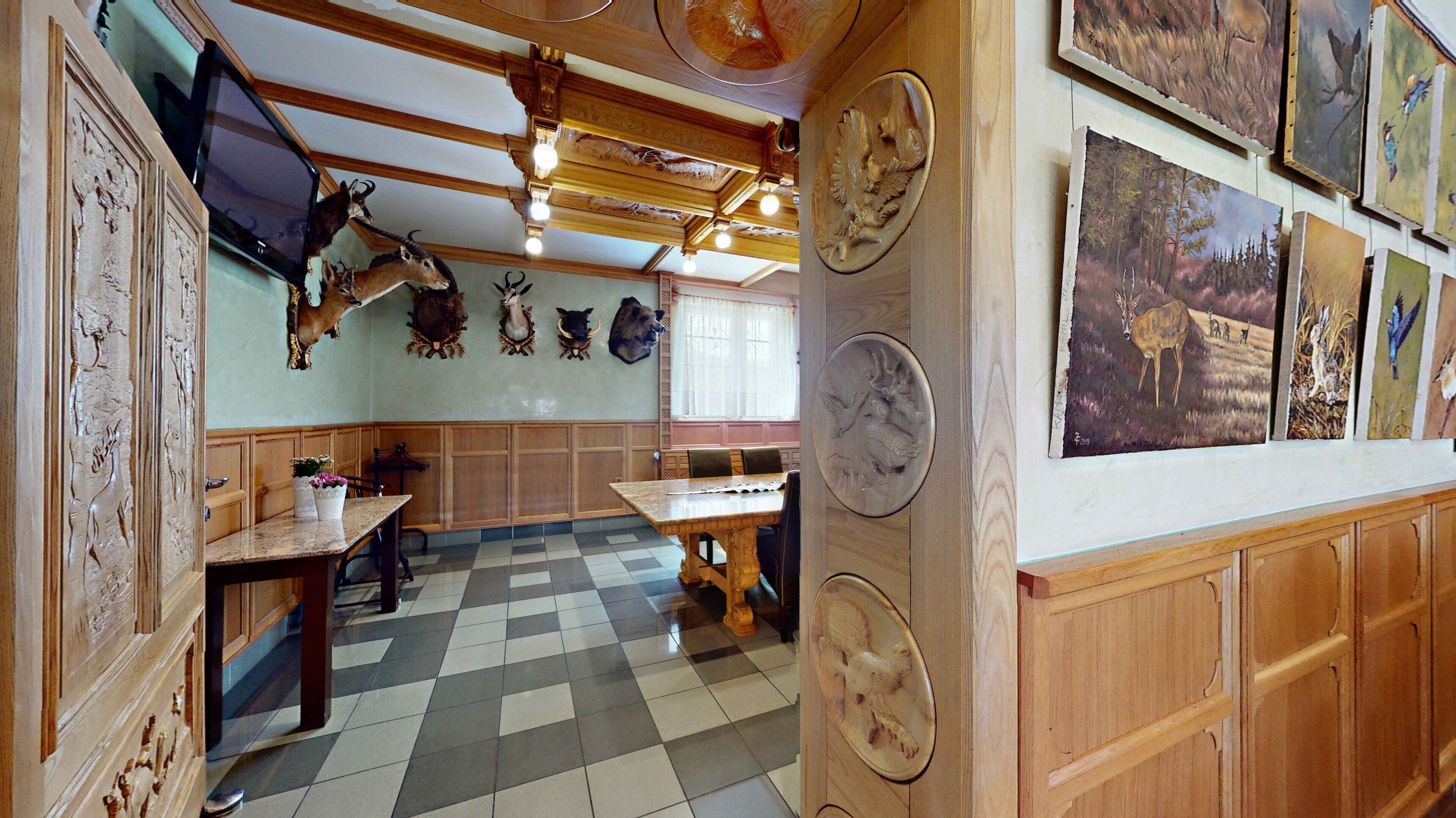 Una habitación con suelo a cuadros, paneles de madera, una mesa de comedor, sillas y cabezas de animales colgadas en la pared.