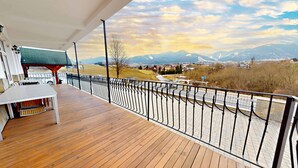 Eine Holzterrasse mit Metallgeländer, das auf eine gebirgige Landschaft blickt.