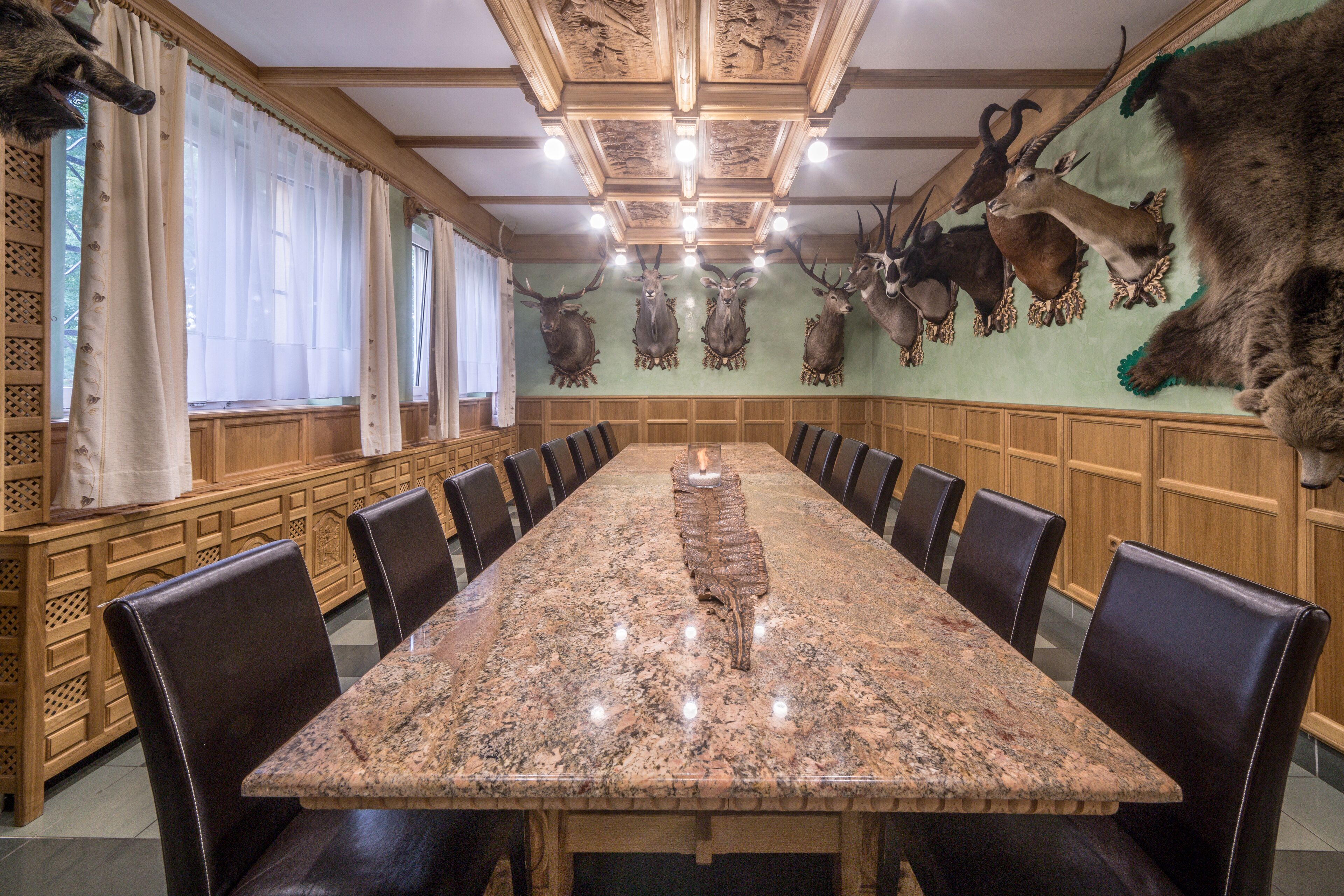 A long dining table with chairs, a chandelier, and mounted animal heads on the wall.