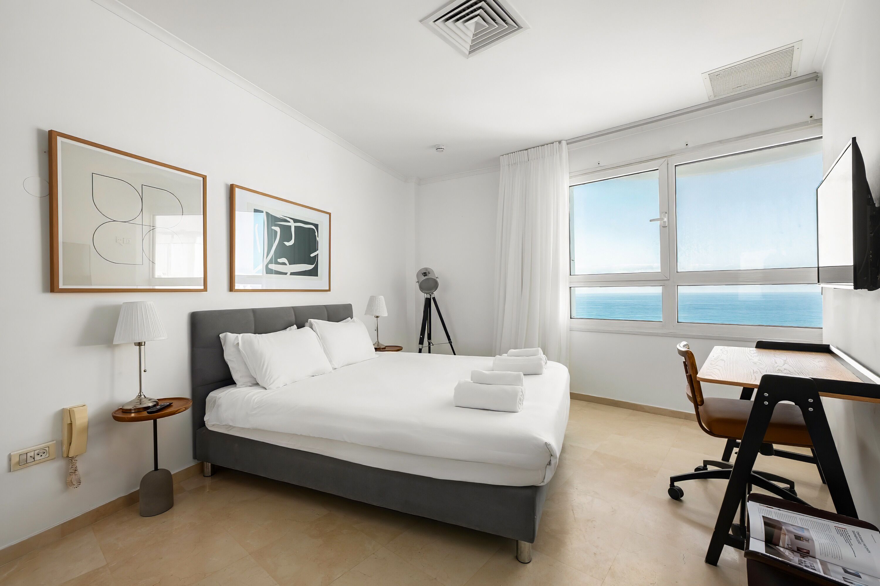 A hotel room with a bed, a desk, a chair, a lamp, a phone, and a window with a view.