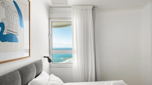 A hotel room with a bed, a window with a view of the sea, and a framed picture on the wall. - Full Sea View on The Beach With Balcony (Tel Aviv)