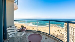 A balcony with a white chair and a pink table, overlooking a beach with clear blue waters and a sandy shore. - Full Sea View on The Beach With Balcony (Tel Aviv)