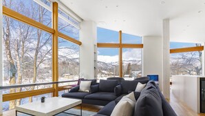 Una sala de estar moderna con un sofá seccional, una mesa de centro y grandes ventanales con vistas a montañas nevadas.