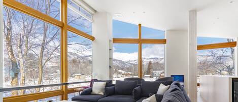 A modern living room with a sectional sofa, a coffee table, and large windows offering a view of snow-covered mountains.