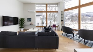 Una sala de estar moderna con un sofá seccional grande, un comedor con mesa y sillas, y un ventanal con vistas a un paisaje nevado.
