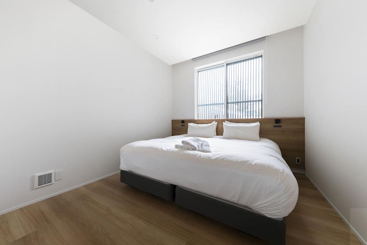 A modern bedroom with a large bed, a window with blinds, and a built-in heater.