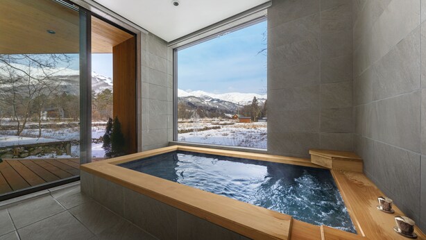 Un baño moderno con un ventanal grande, una bañera de madera y vistas a montañas nevadas.