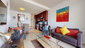 A modern living room with a sofa, armchair, coffee table, and a dining area. - Portico Beachfront Condo (Cape Town)