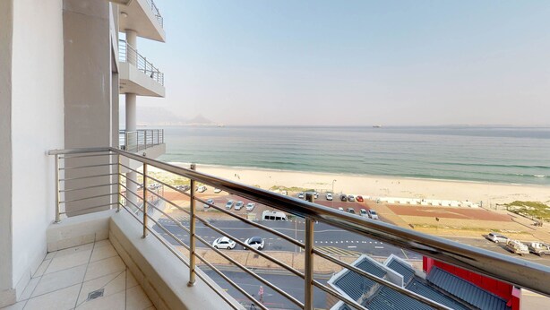 A balcony with a view of a beach and parking area. - Portico Beachfront Condo (Cape Town)