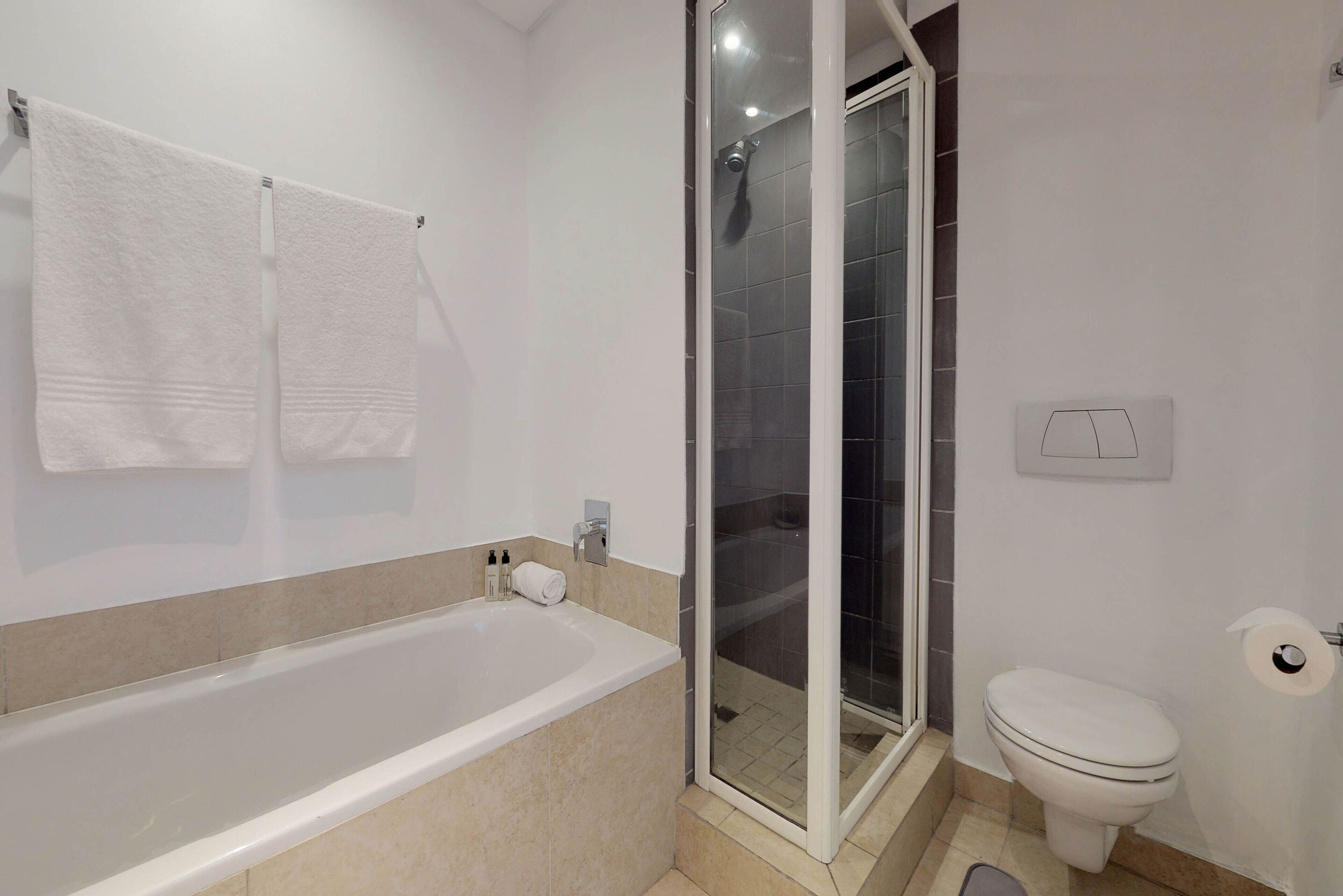 A bathroom with a bathtub, a glass-enclosed shower, a toilet, and two towels hanging on the wall.