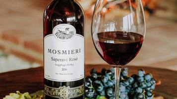 A bottle of Mosmieri Saperavi Rosé wine and a glass of red wine on a table with a glass plate, surrounded by grapes and corks.