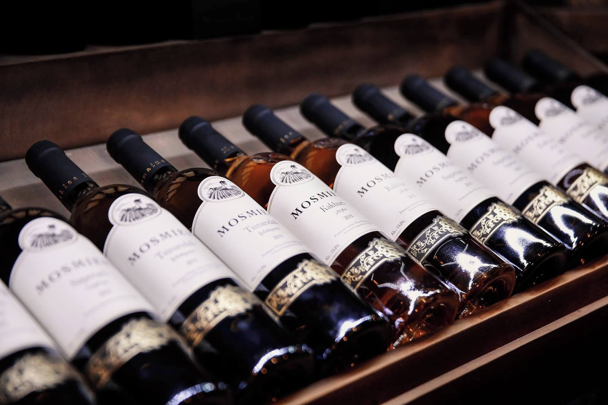Una hilera de botellas de vino con etiquetas, dispuestas sobre una superficie de madera.