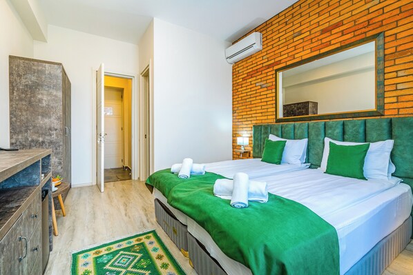 Ein Hotelzimmer mit einer Ziegelwand, einem großen Bett mit grüner Bettwäsche, einem hölzernen Schminktisch und einem Teppich mit grünem Muster.