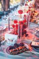 A table set for a meal with plates of food, glasses, and a vase with red flowers.