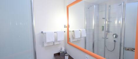 A modern bathroom with a glass shower enclosure, a large mirror with an orange frame, and a wooden vanity.