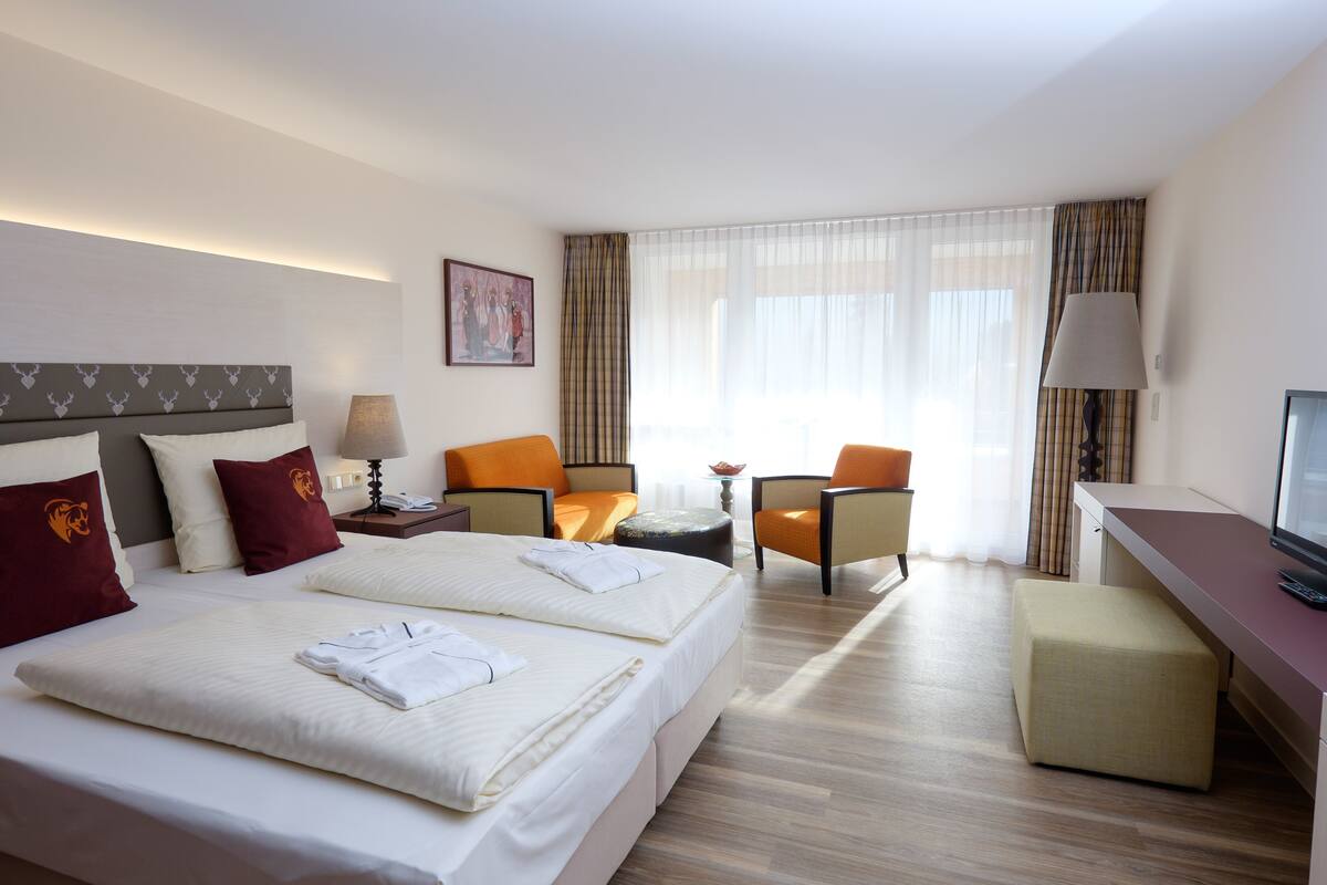 A hotel room with two beds, a desk, a chair, a TV, and a window with curtains.