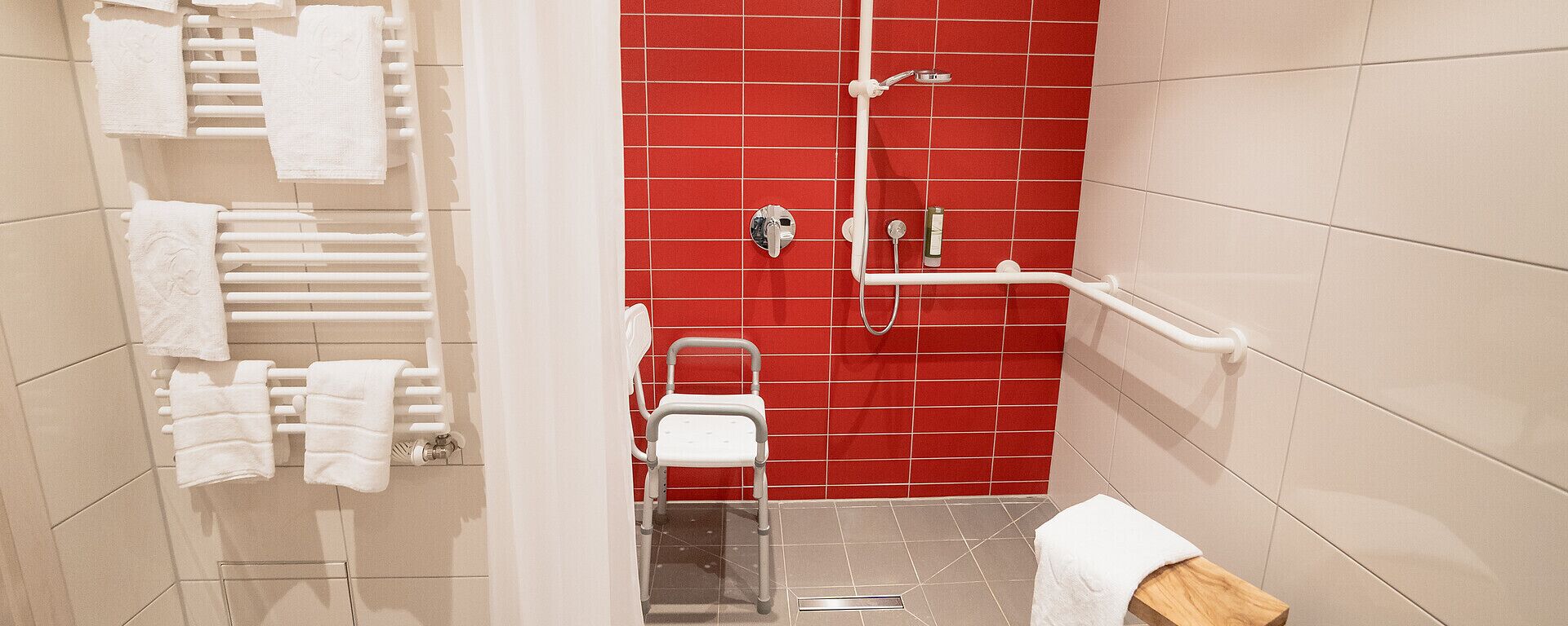 Une salle de bain avec un mur recouvert de carreaux rouges, un porte-serviettes blanc, une chaise blanche et un espace douche.