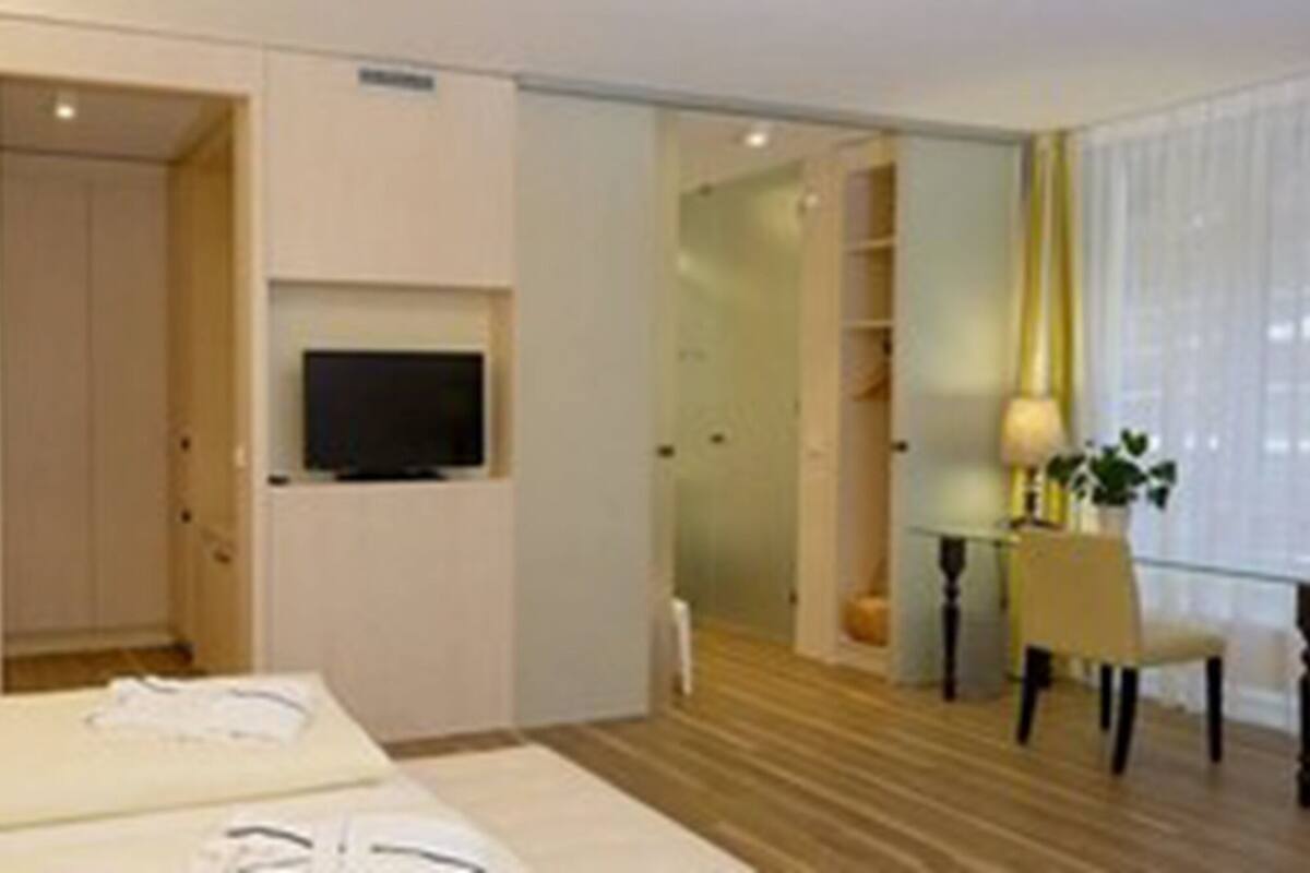 A hotel room with a bed, a television, a desk with a chair, and a window with curtains.