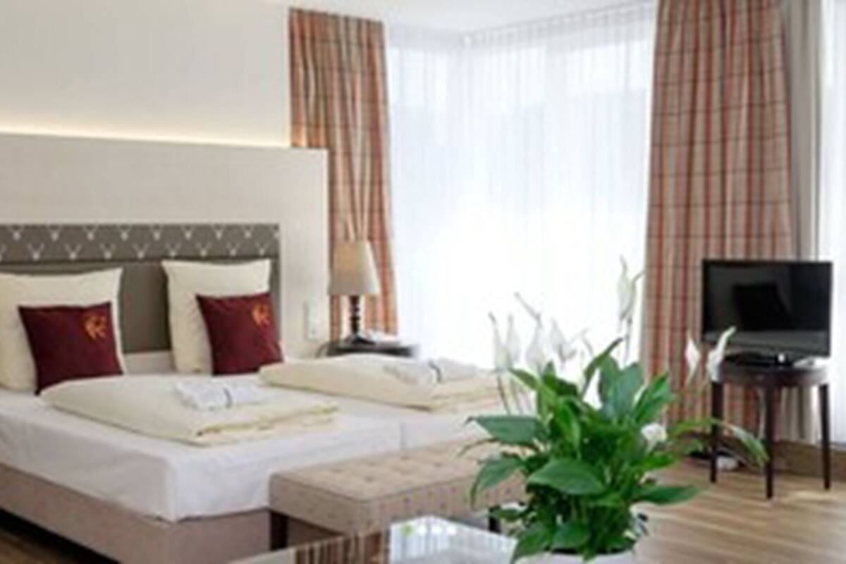 A hotel room with a bed, a TV, a chair, and a plant.