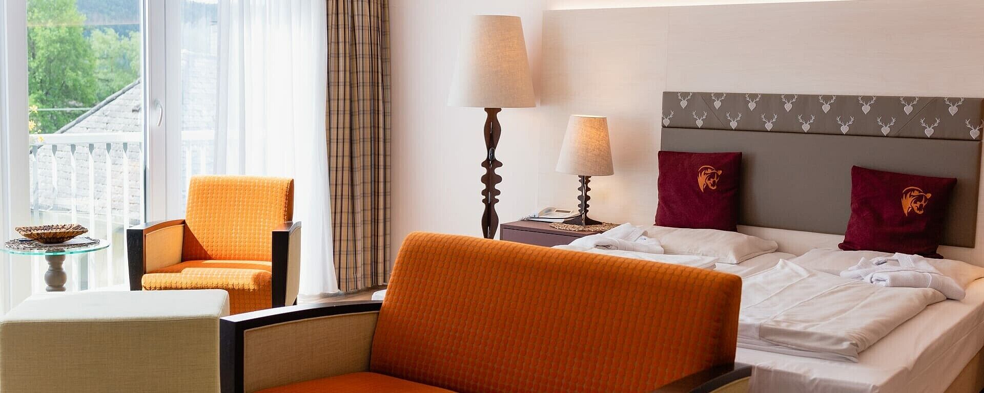 A hotel room with a bed, two chairs, a lamp, and a view of the outdoors.