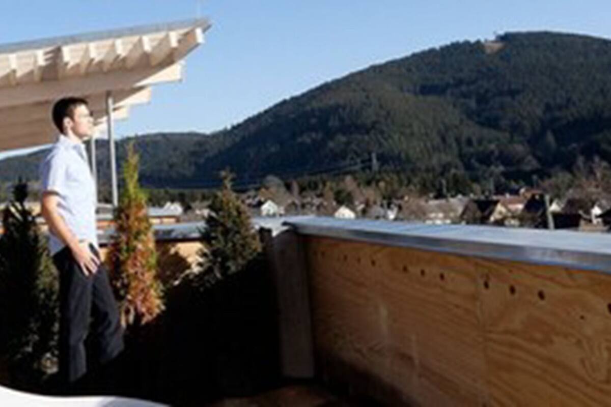 A man standing on a balcony with a view of a mountain and a building in the background.