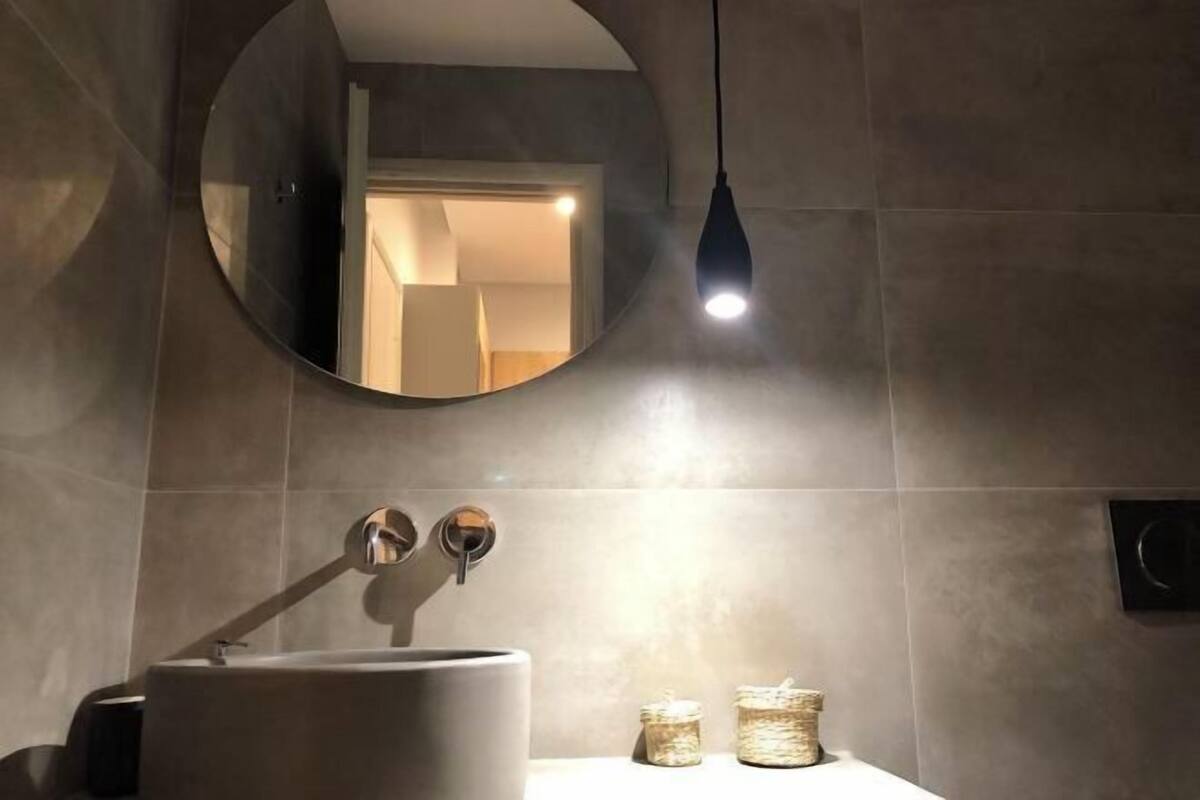 A bathroom with a round mirror, a sink, and two jars on the counter.