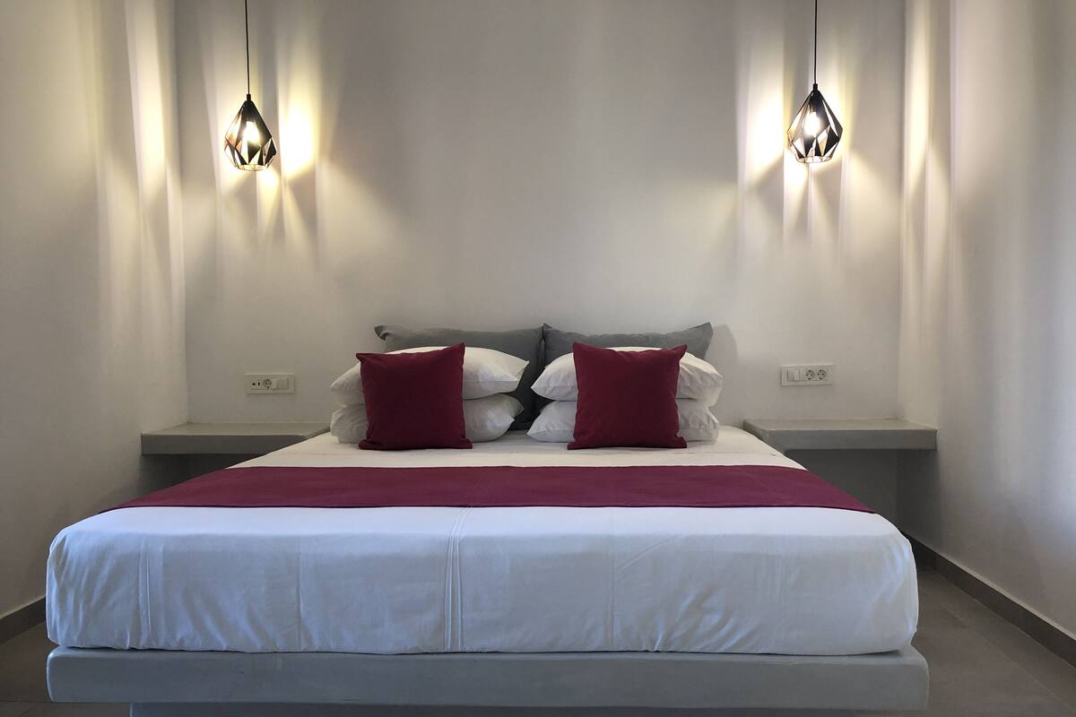 A modern bedroom with a large bed, two bedside tables, and two pendant lights.