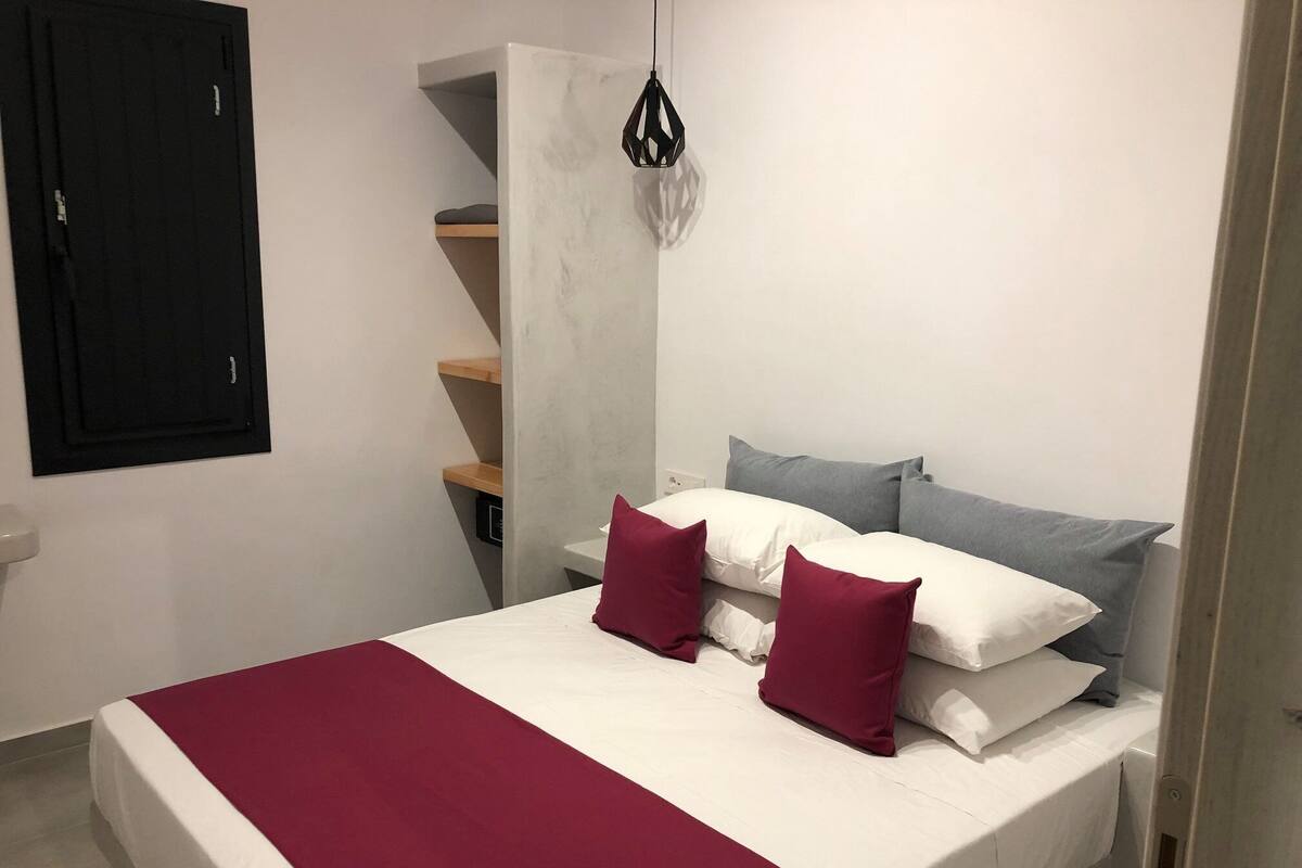 A bedroom with a bed, pillows, a hanging light, and a wardrobe.