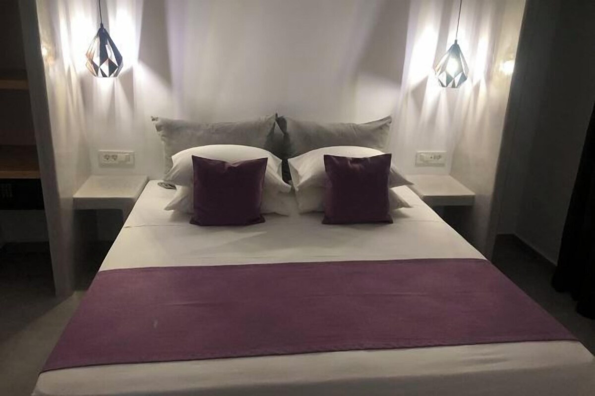 A bed with two pillows, a purple blanket, and two bedside tables with lamps.