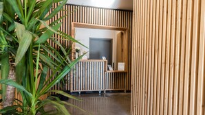 A reception area with a wooden reception desk, a door, and a plant. - Le H85 (Chatte)