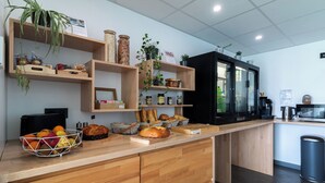 A modern kitchen with wooden cabinets, a countertop with a fruit bowl, bread, and jars. - Le H85 (Chatte)