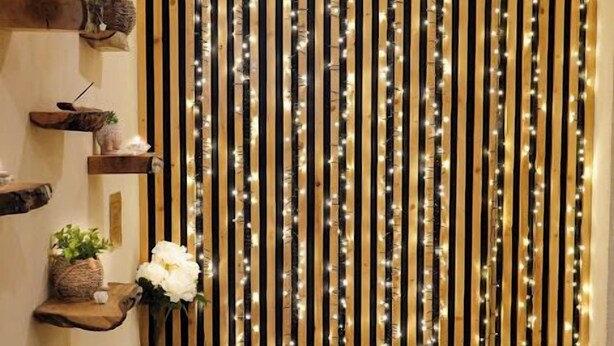 A hallway with wooden floors, a bench, and a wall decorated with vertical wooden slats and string lights. - Le H85 (Chatte)