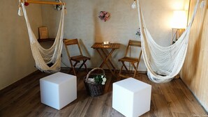 A room with two hammocks, wooden chairs, a small table with a candle, and white storage cubes. - Le H85 (Chatte)
