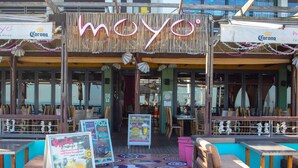 A restaurant with outdoor seating, a wooden facade, and signs advertising promotions. - Eden on the Bay Apartment 67B (Cape Town)