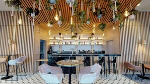 A modern bar area with a wooden ceiling, hanging plants, and a bar counter with various bottles. There are two round tables with chairs in the foreground. - voco Manchester City Centre by IHG (Manchester)