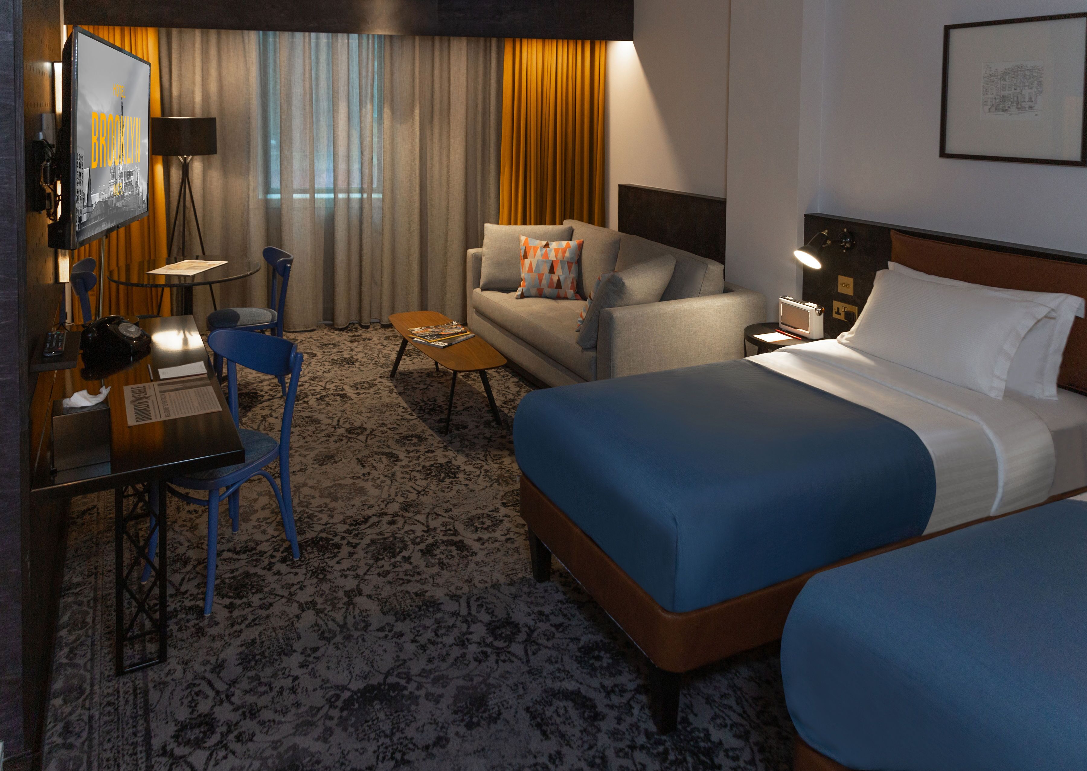 A hotel room with a large bed, a sofa, a desk with a chair, a small table, and a TV.