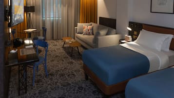 A hotel room with a large bed, a sofa, a desk with a chair, a small table, and a TV.