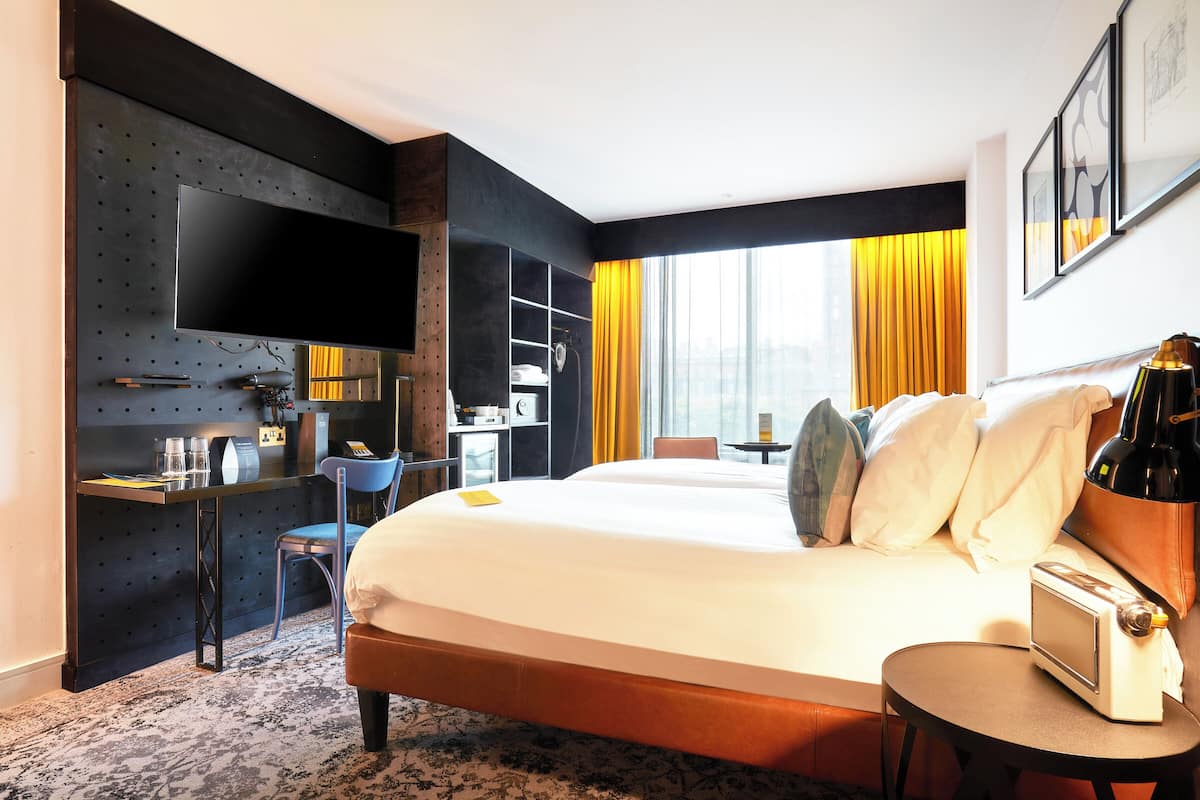 A hotel room with a bed, a desk with a flat-screen TV, a small table with a toaster, and a chair.
