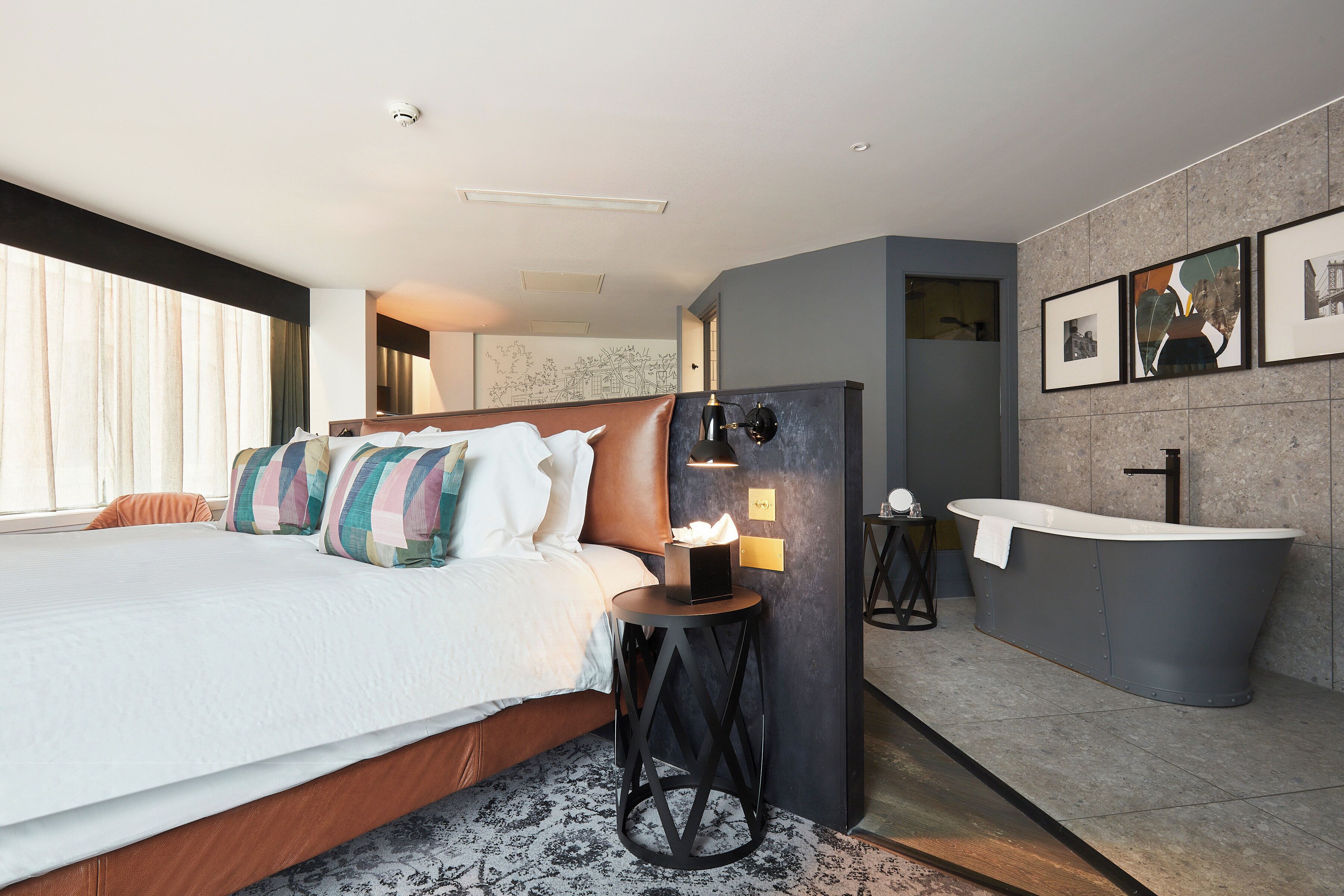 A modern hotel room with a large bed, a round side table, a bathtub, and a wall-mounted sink.