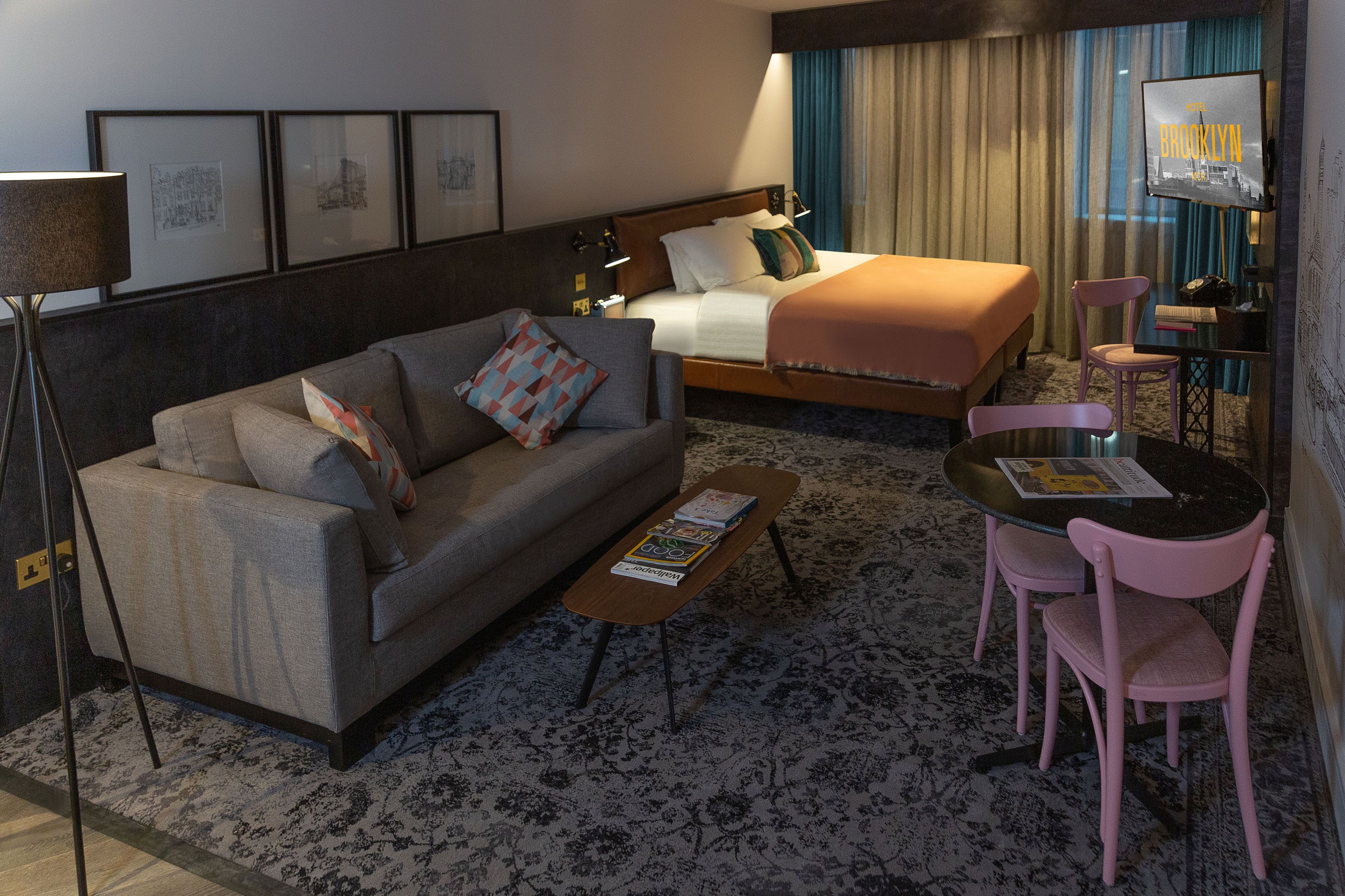 Quarto de hotel com cama, sofá, mesa de centro e televisão.