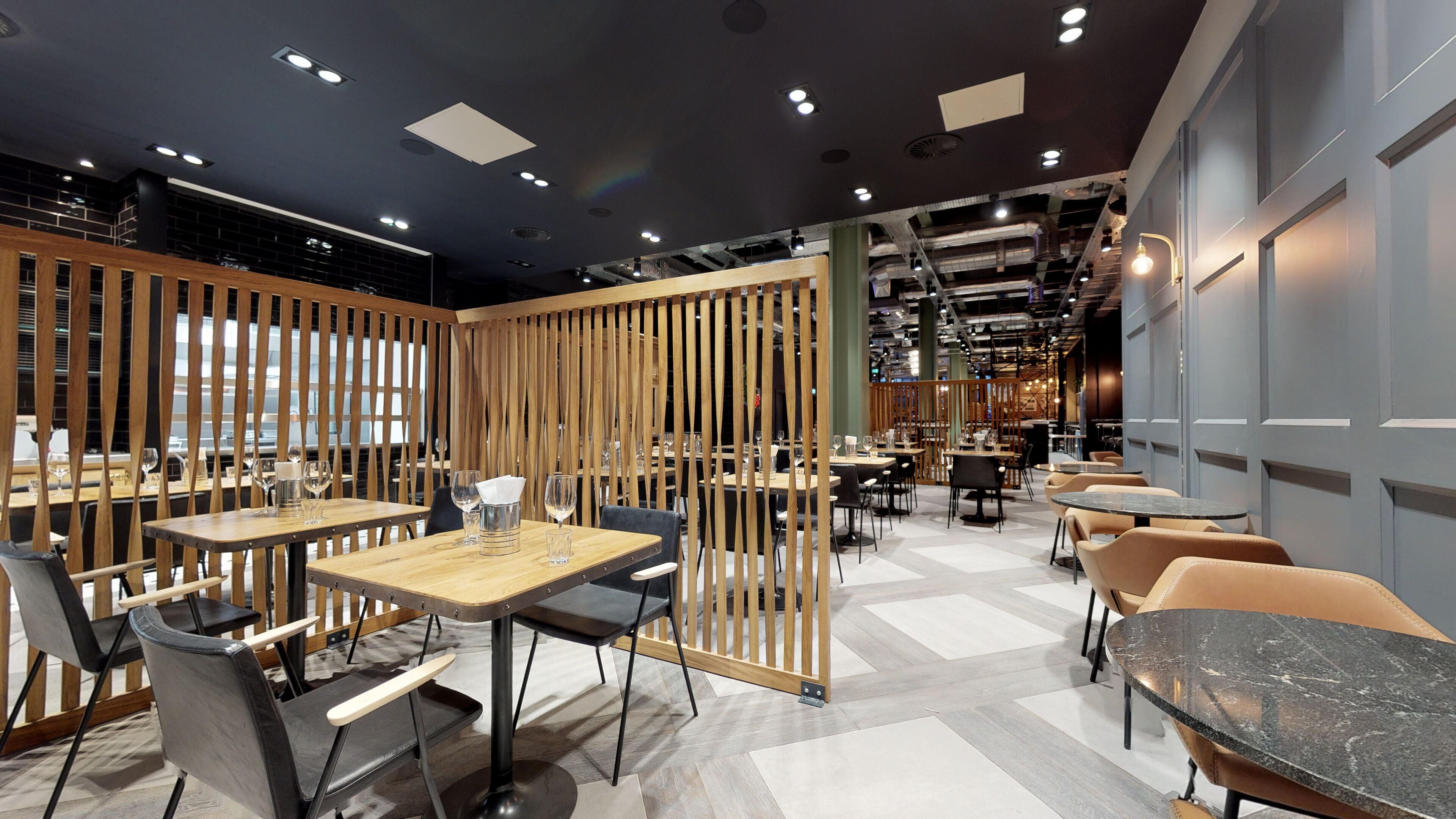 A modern restaurant interior with wooden partitions, multiple dining tables, and chairs.
