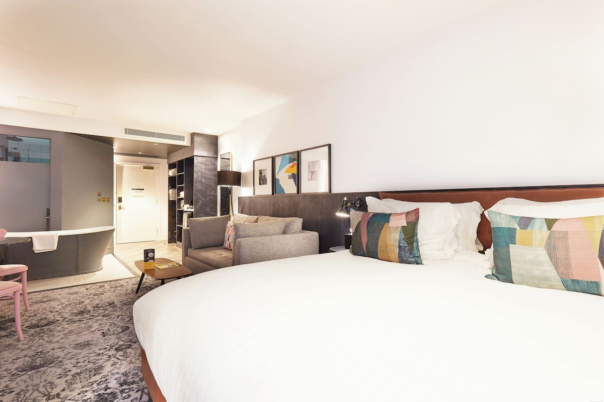 A hotel room with a large bed, a sofa, a desk, and a bathroom.