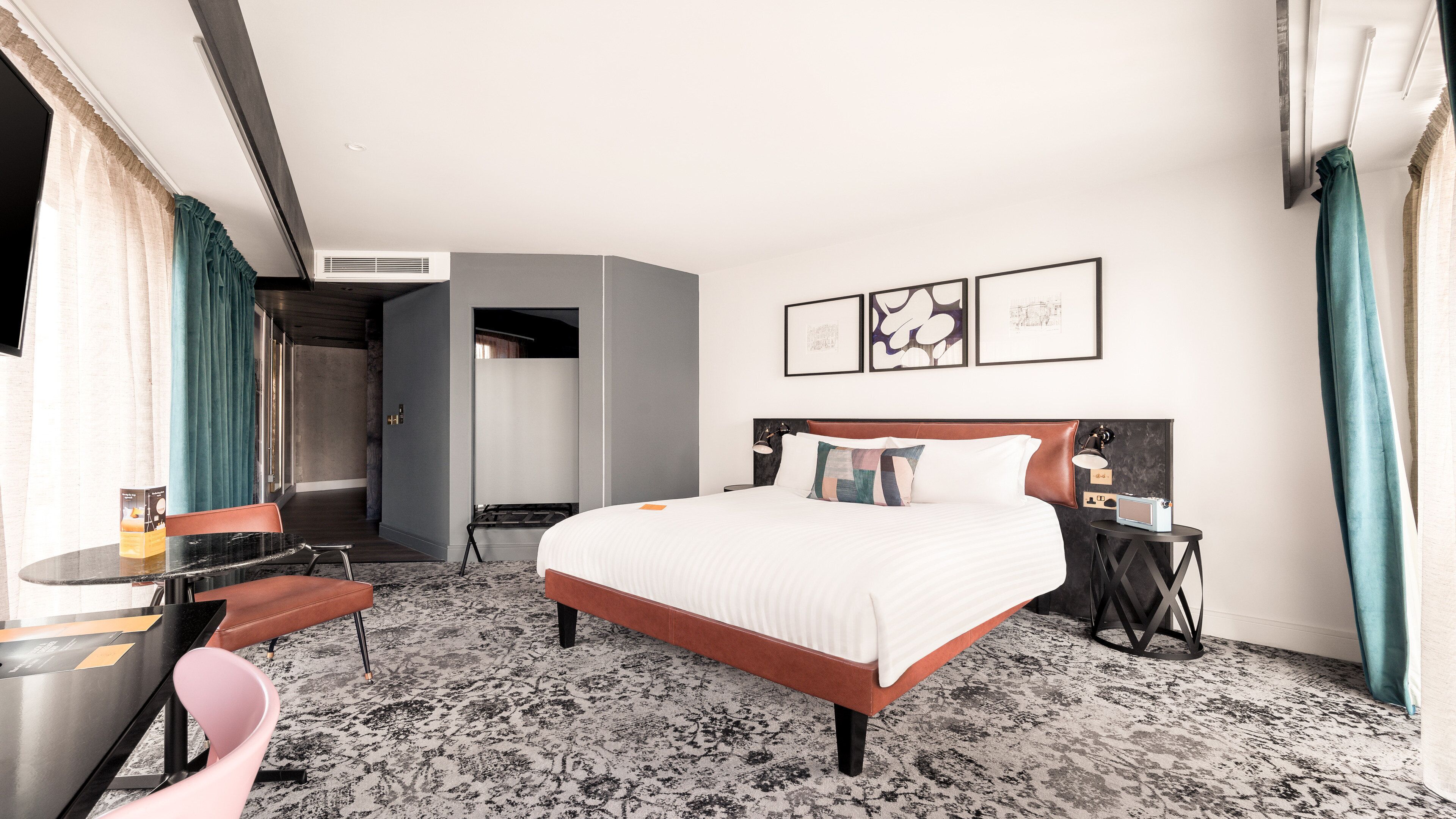 Habitació d'hotel amb llit, escriptori, cadira, taula petita i ràdio penjada a la paret.