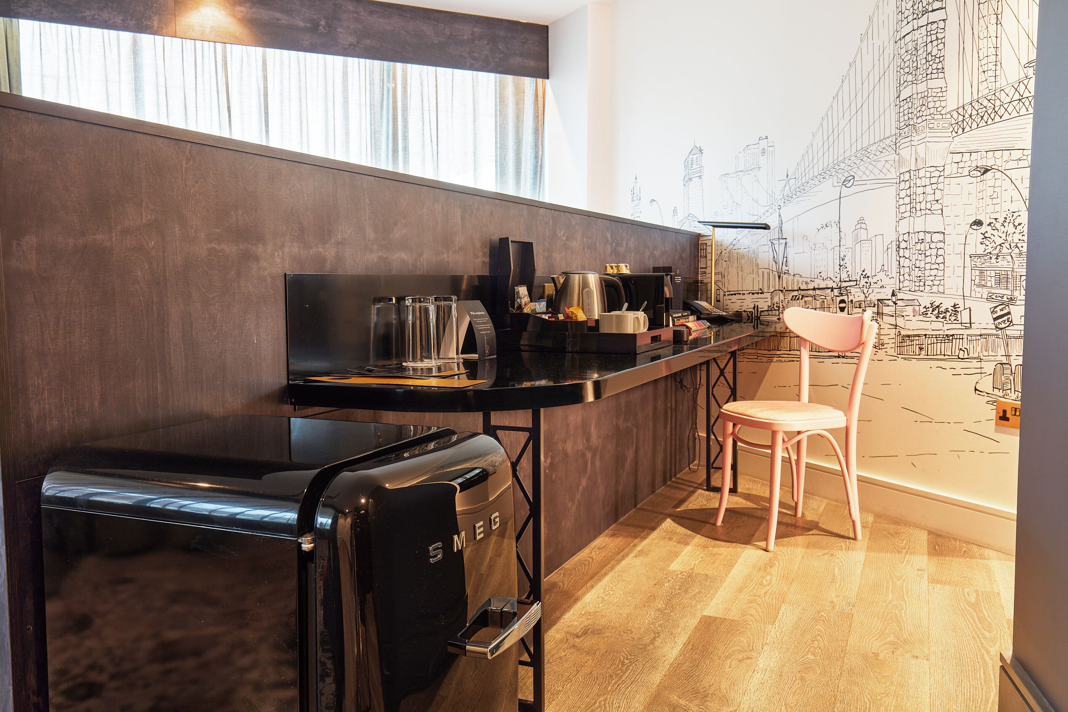 Cocina compacta con cafetera, hervidor y tostadora. Hay una silla y una mesita con una jarra de café y tazas.