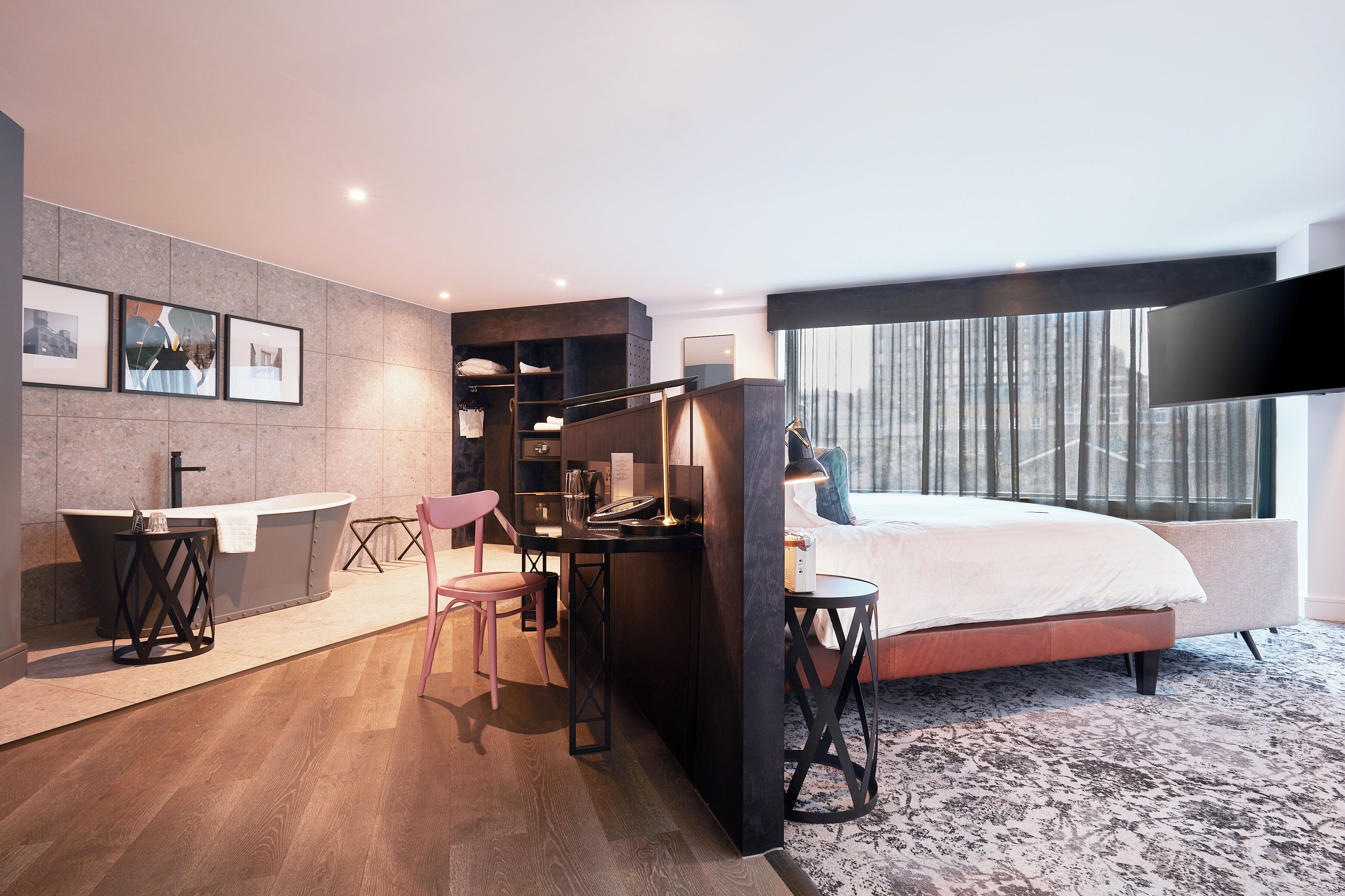 Et moderne hotelværelse med en stor seng, et skrivebord med stol, et lille bord, et sminkebord med spejl og billeder i rammer på væggen.