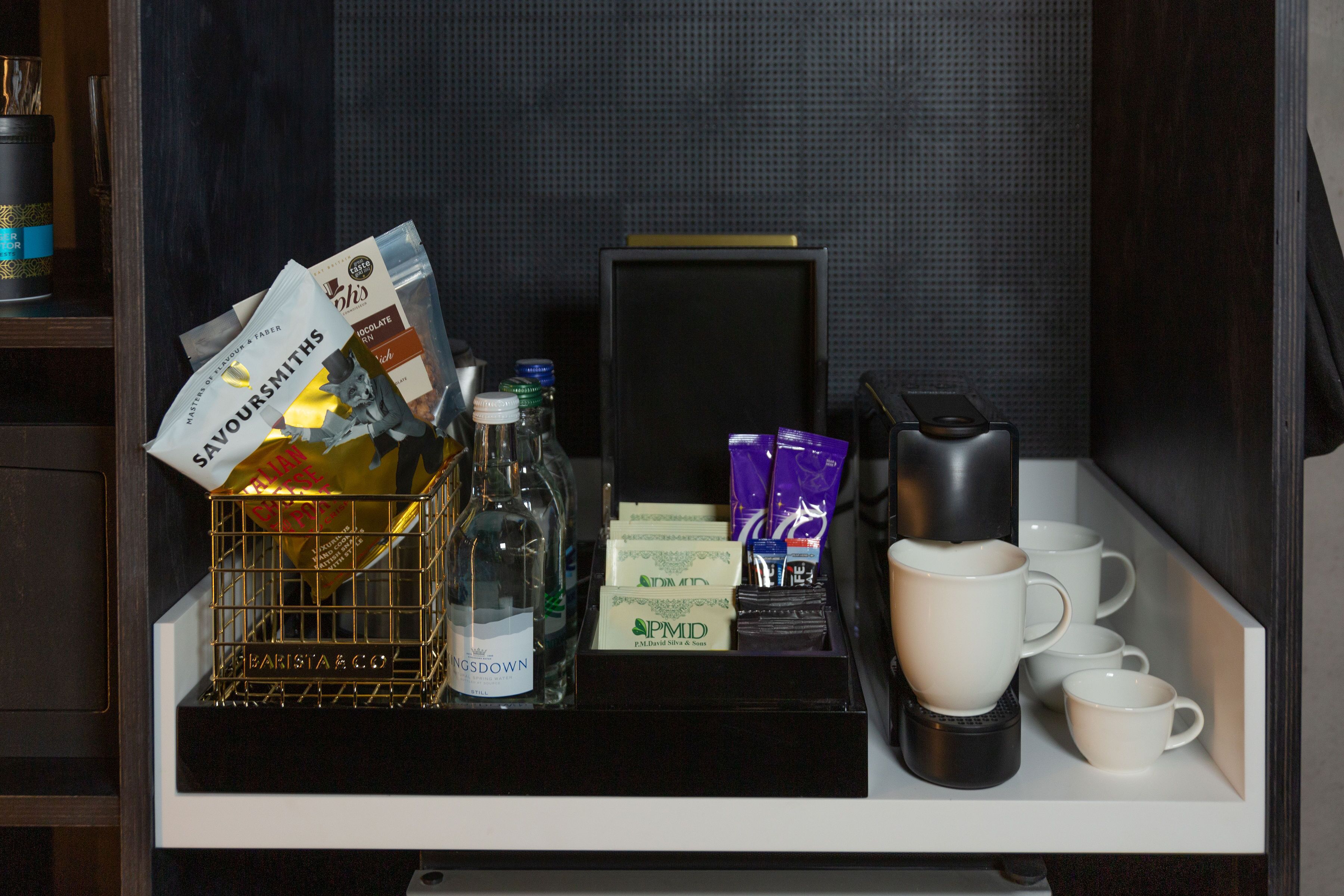 A minibar with a bottle of water, a glass of wine, a coffee maker, and several cups.