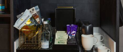 A minibar with a bottle of water, a glass of wine, a coffee maker, and several cups.